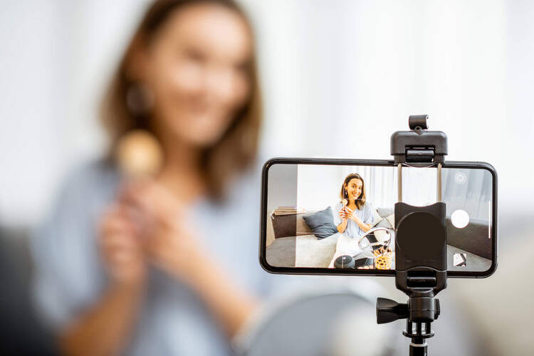 Frau filmt sich selbst und hält Produkt in Kamera