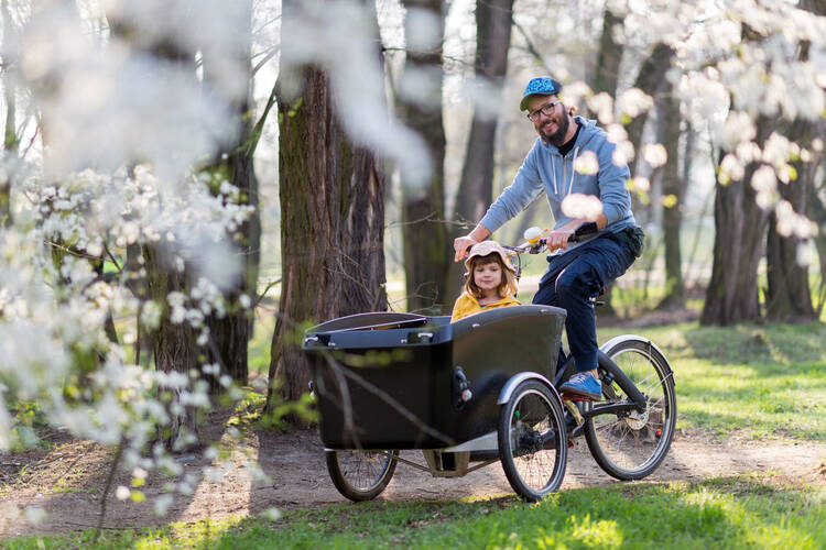 Person fährt Kinder in einem Lastenrad durch den Park