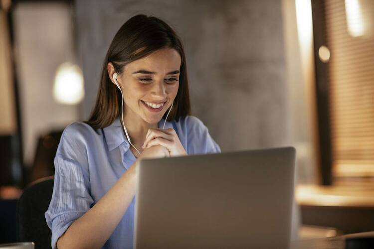 Frau im Hemd sitzt lächelnd vor Laptop und kommuniziert