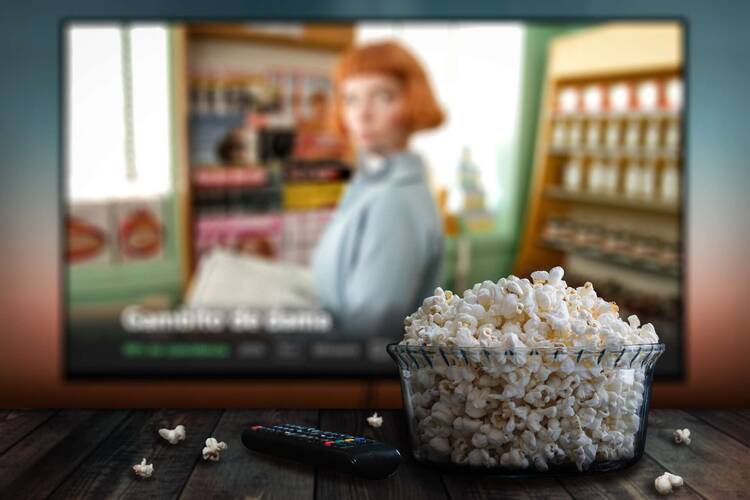 Fernseher im Hintergrund mit Netflix Programm, im Vordergrund eine Schüssel Popcorn und eine Fernbedienung