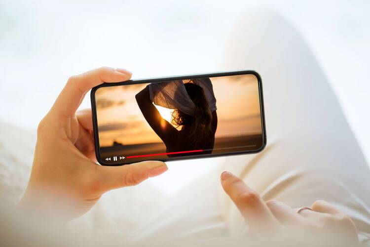 Zwei Hände halten Smartphone, auf dem ein Video abgespielt wird