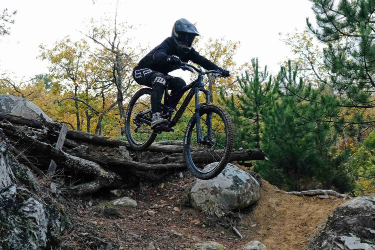 Frau fährt mit Mountainbike durch Wald einen Abhang hinunter.