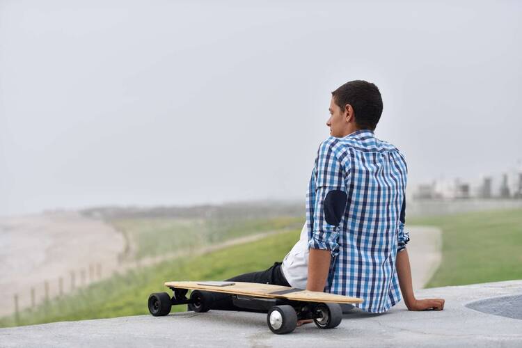 Mann sitzt auf dem Boden und neben ihm steht ein E-Skateboard