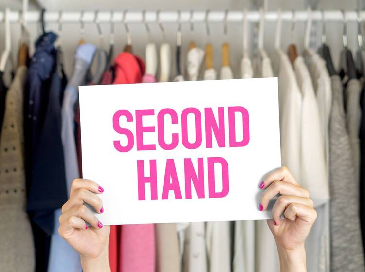 Schild mit "Second Hand"-Aufschrift wird vor Kleidung gehalten