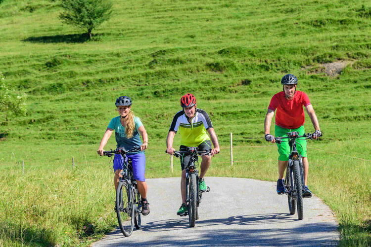 Drei Personen fahren mit Fahrrad über den Radweg durch einer Wiese.