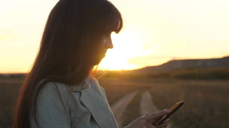 Frau steht in der Natur mit iPhone in der Hand