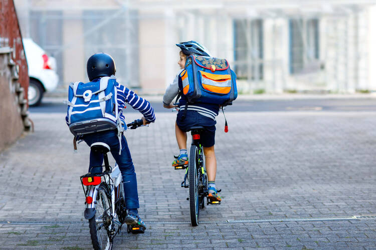 zwei Kinder fahren mit Helm und Rucksack zur Schule
