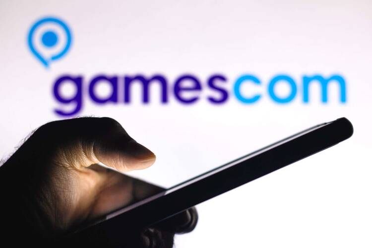 Hand hält Smartphone vor Gamescom Schriftzug auf weißem Hintergrund