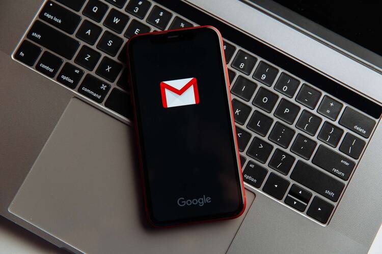 Smartphone mit geöffneter Gmail Applikation liegt geöffnet auf Macbook-Tastatur