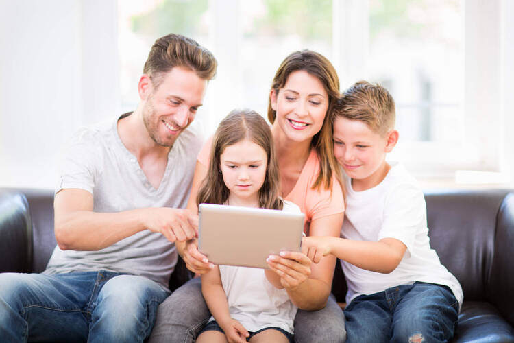 Familie sitzt lächelnd vor Tablet
