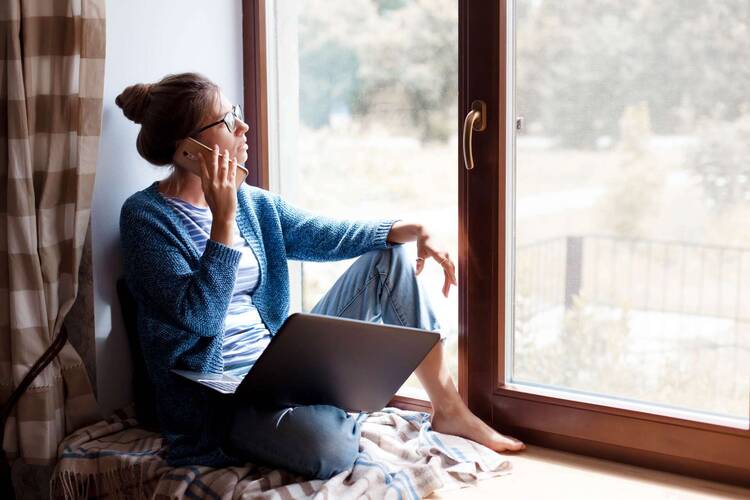 Frau sitzt gemütlich vor Fenster mit Laptop auf dem Schoß