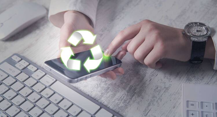 Hände tippen auf Smartphone Display mit darüber schwebendem Recycling-Hologramm vor Tastatur