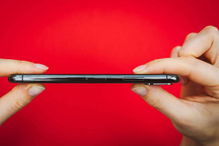 Smartphone wird zwischen zwei Händen gehalten vor rotem Hintergrund