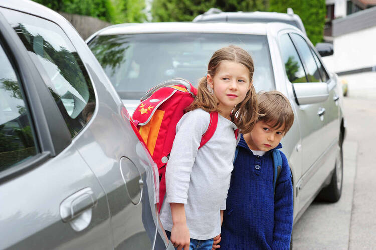 zwei Kinder zwischen Autos schauen vorsichtig auf die Straße