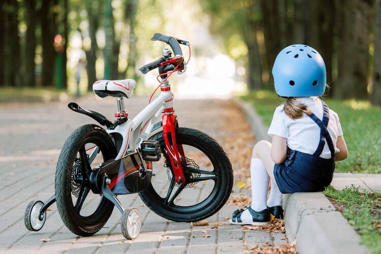 Kind mit Helm sitzt neben Fahrrad auf Bordstein.
