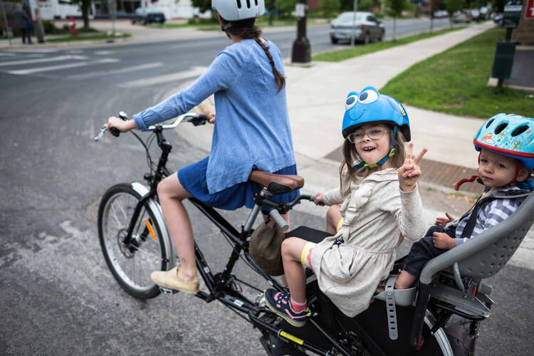 Frau fährt mit zwei Kindern auf einem Lastenrad und alle tragen einen Helm