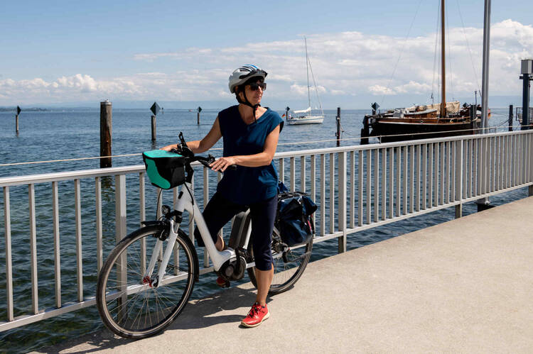 Frau steht neben Ihrem E-Bike auf dem Steg von einem See.