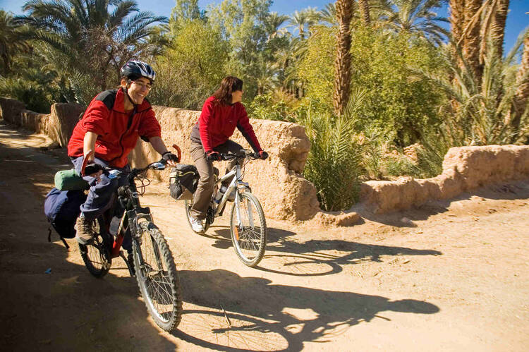 Zwei Frauen fahren auf Fahrrad über trockenen Weg in Marokko.