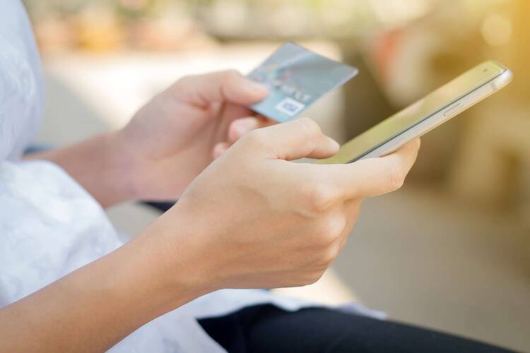 Person hält in einer Hand Smartphone, in anderer Hand Bankkarte