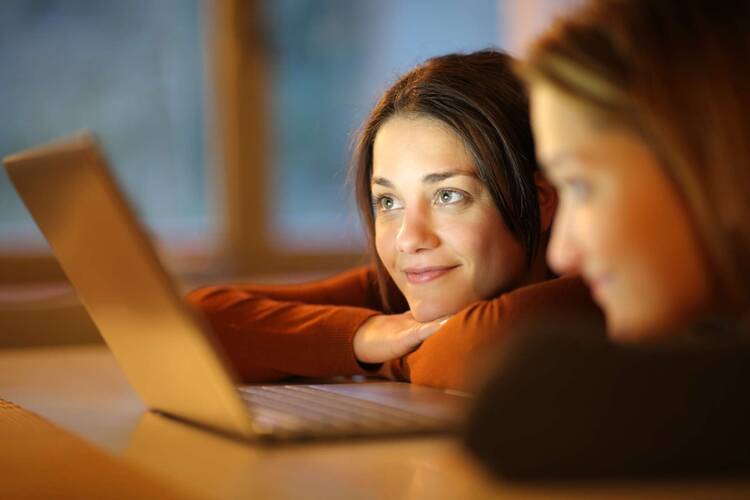 Zwei Frauen liegen lächelnd vor Laptop