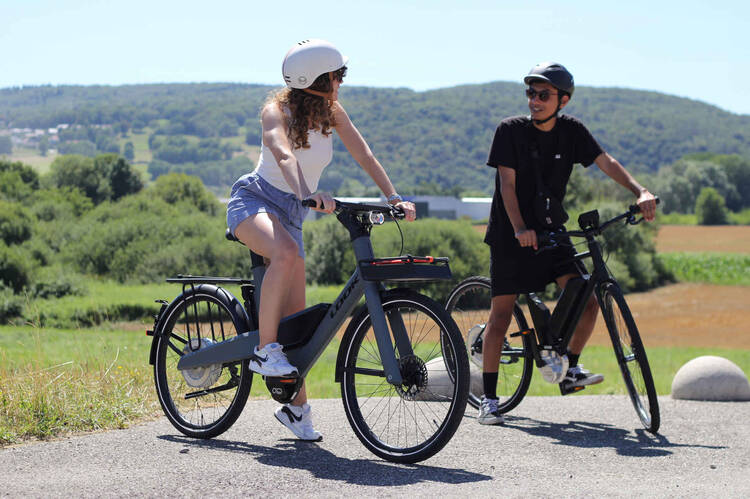 Mann und Frau mit Helm und Fahrrad vor grüner Landschaft.