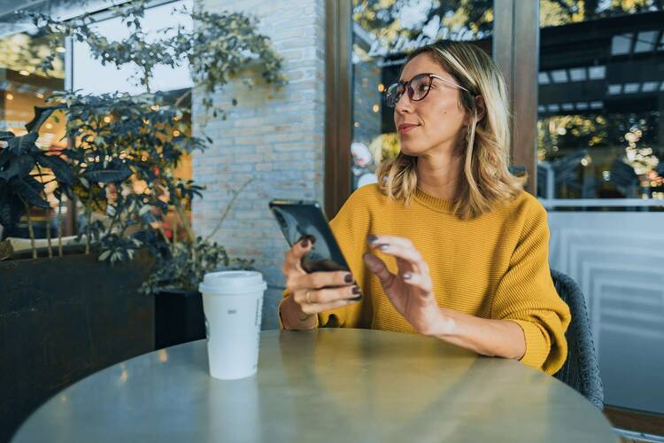 Frau im gelben Pulli in Café hält Smartphone in der Hand