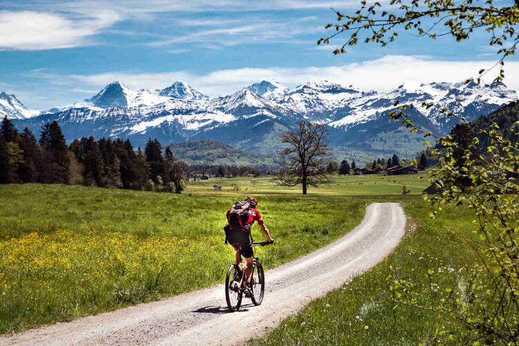 Mann fährt auf Fahrrad durch schöne Landschaft vor Bergkette