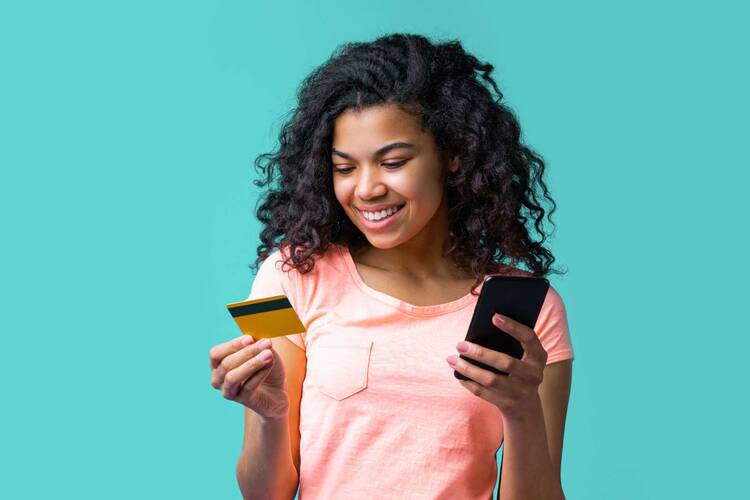 Frau schaut lächelnd auf Kreditkarte in der Hand mit Smartphone in der anderen Hand