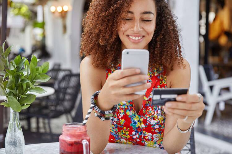 Frau schaut lächelnd auf Smartphone in einer Hand und Bankkarte in anderer Hand
