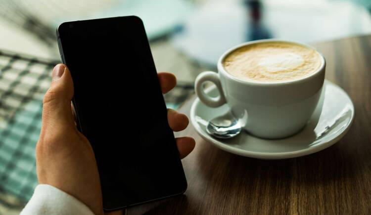 Handy wird neben Kaffeetasse gehalten