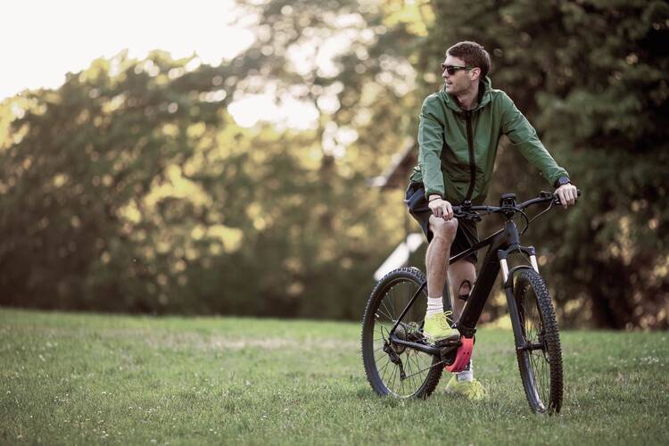 Mann steht mit Fahrrad auf einer Wiese