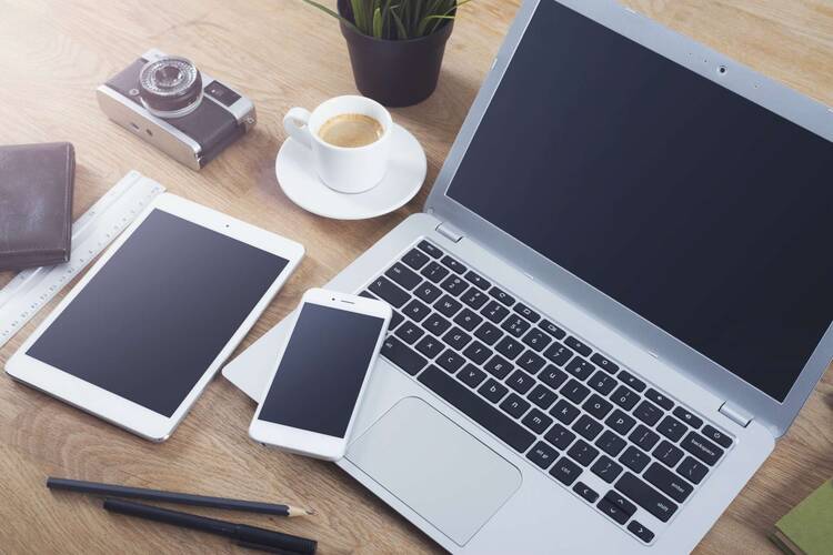 Laptop, Smartphone und Tablet auf einem Tisch mit weiteren Gegenständen