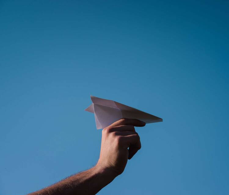 Papierflieger wird von Hand vor blauem Himmel gehalten