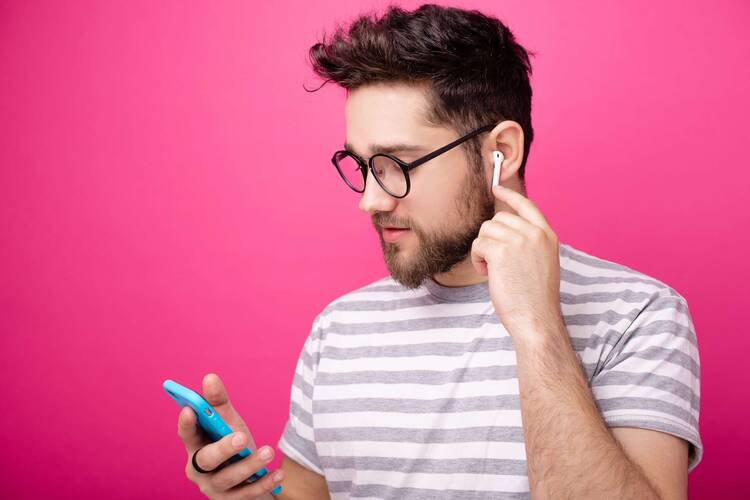Mann guckt mit AirPods in den Ohren auf Smartphone