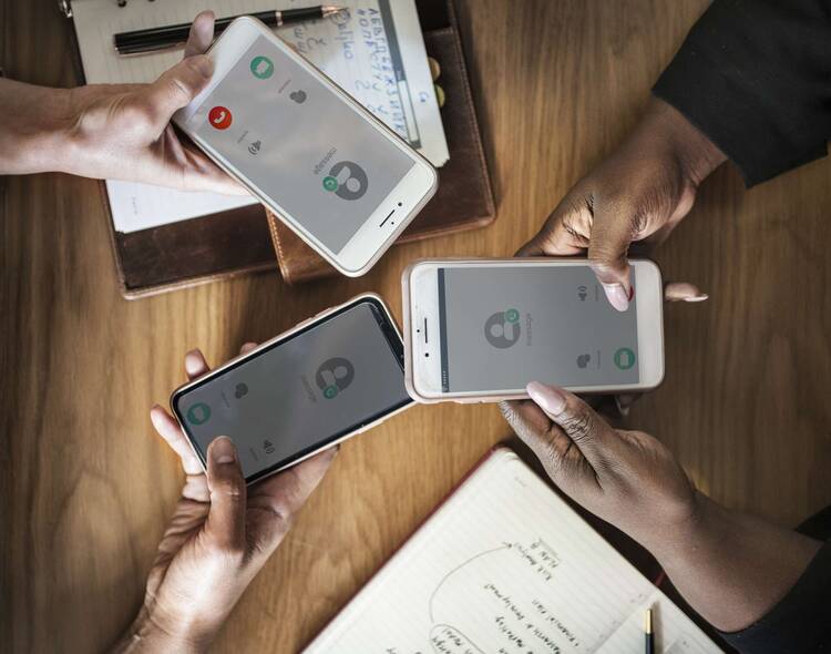 Drei Hände halten drei Smartphones mit WhatsApp Gruppenanruf auf Display zusammen in die Mitte