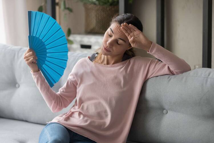 Frau auf Couch nutzt blauen Fächer für frische Luft