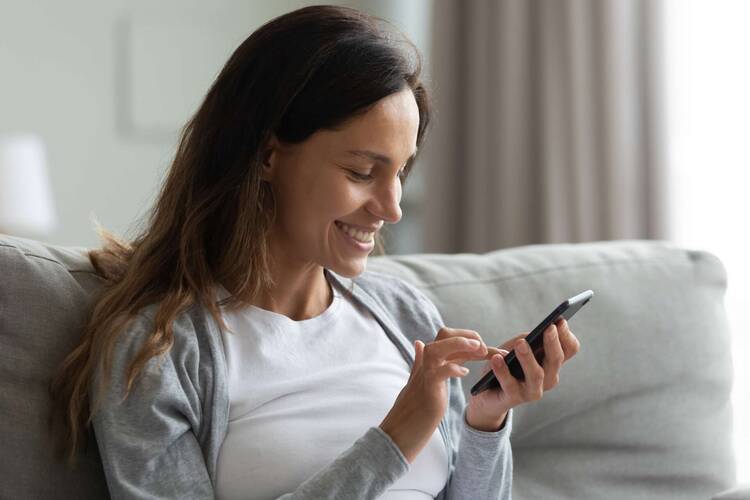 Frau sitzt auf Couch und schaut lächelnd auf Smartphone