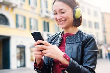 Frau schaut fröhlich Musik mit Kopfhörern hörend auf Smartphone Display