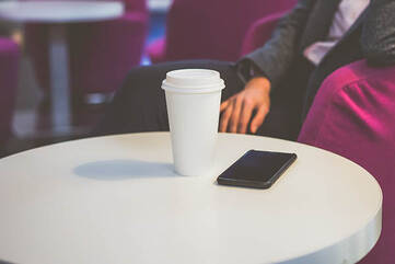 Schwarzes Smartphone mit Kaffeebecher auf einem Tisch