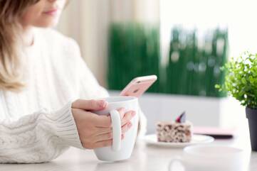 Frau genießt Kaffee und Kuchen, während sie aufs iPhone schaut 