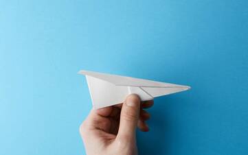 Ein kleiner Papierfliegerwird vor einem blauen Hintergrund gehalten
