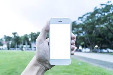 iPhone gehalten von Hand vor einer Grasfläche