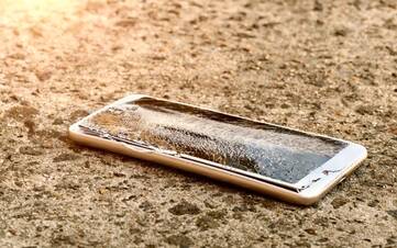 Smartphone mit gebrochenem Display liegt auf Sand