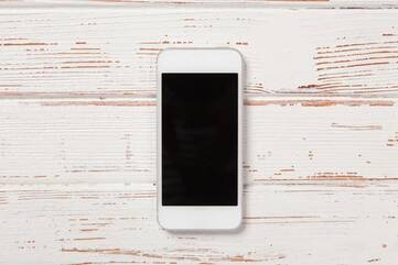 Weißes Smartphone liegt auf hölzerner Unterlage