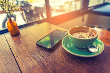 Schwarzes Smartphone mit Kaffeetasse auf Holztisch