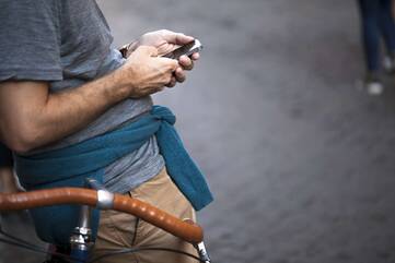 Person lehnt an Fahrrad und bedient mit zwei Händen Smartphone