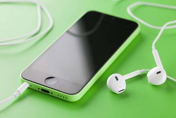 Ein iPhone liegt mit angesteckten Kopfhörern auf einer grünen Fläche