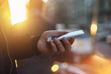 Smartphone gehalten in der linken Hand vor Sonneneinstrahlung aus dem Hintergrund