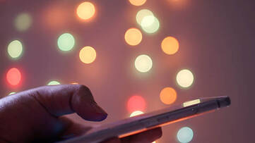 Smartphone gehalten in einer Hand vor einem Hintergrund mit unscharfen bunten Lichtern