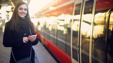 Frau steht vor Zug mit Smartphone in der Hand